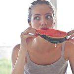 Portrait of a woman eating watermelon indoors, reflecting health and summer vibes.